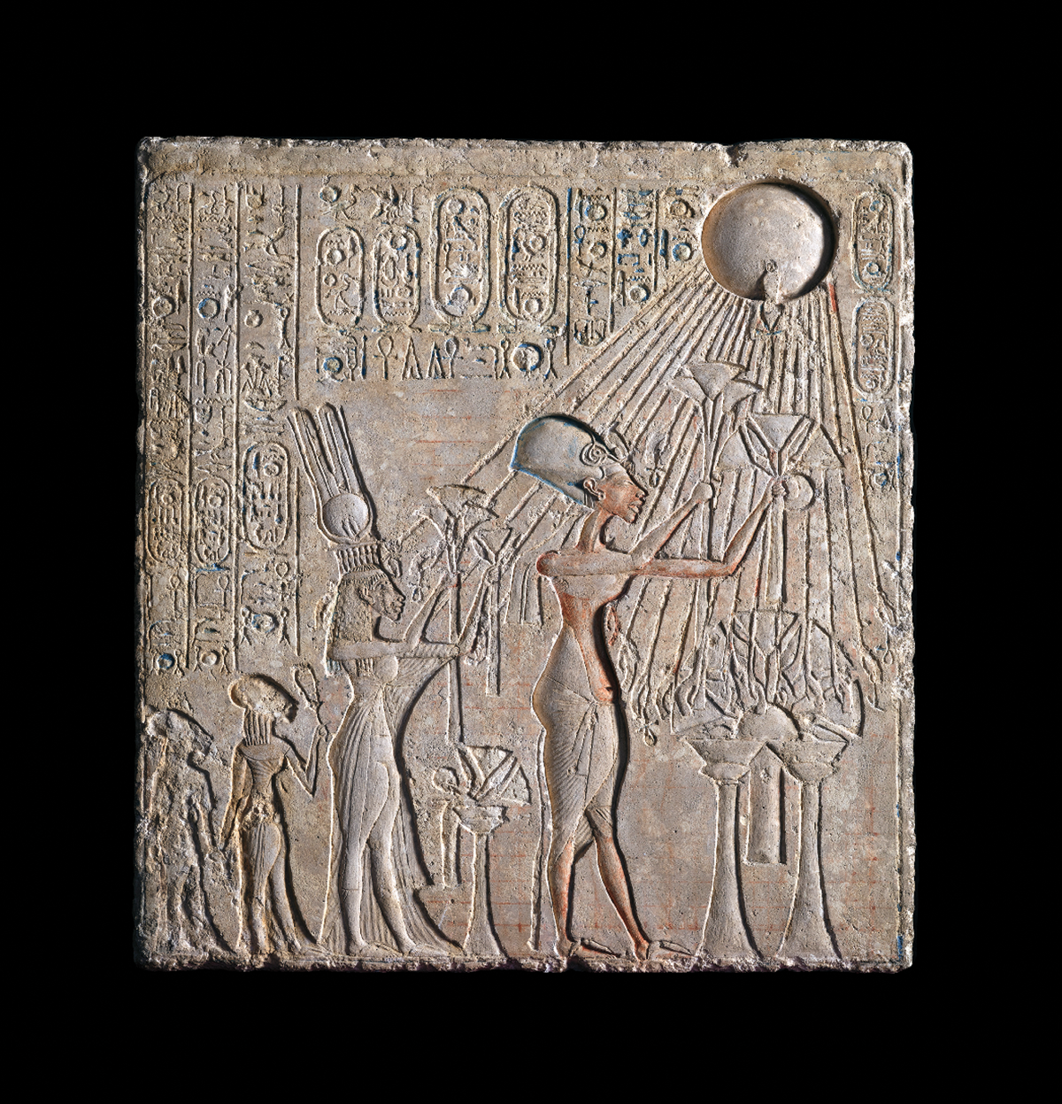 photo of ornately carved stone stela with hieroglyphics, round sun with rays, and several figures, with traces of original paint remaining on the figure of Akhenaten