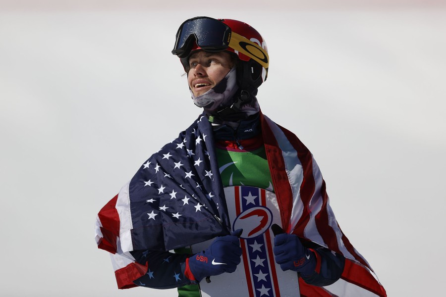 A snowboarder with an American flag draped around his shoulders