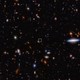 A field of thousands of small galaxies of various shapes and colors on the black background of space