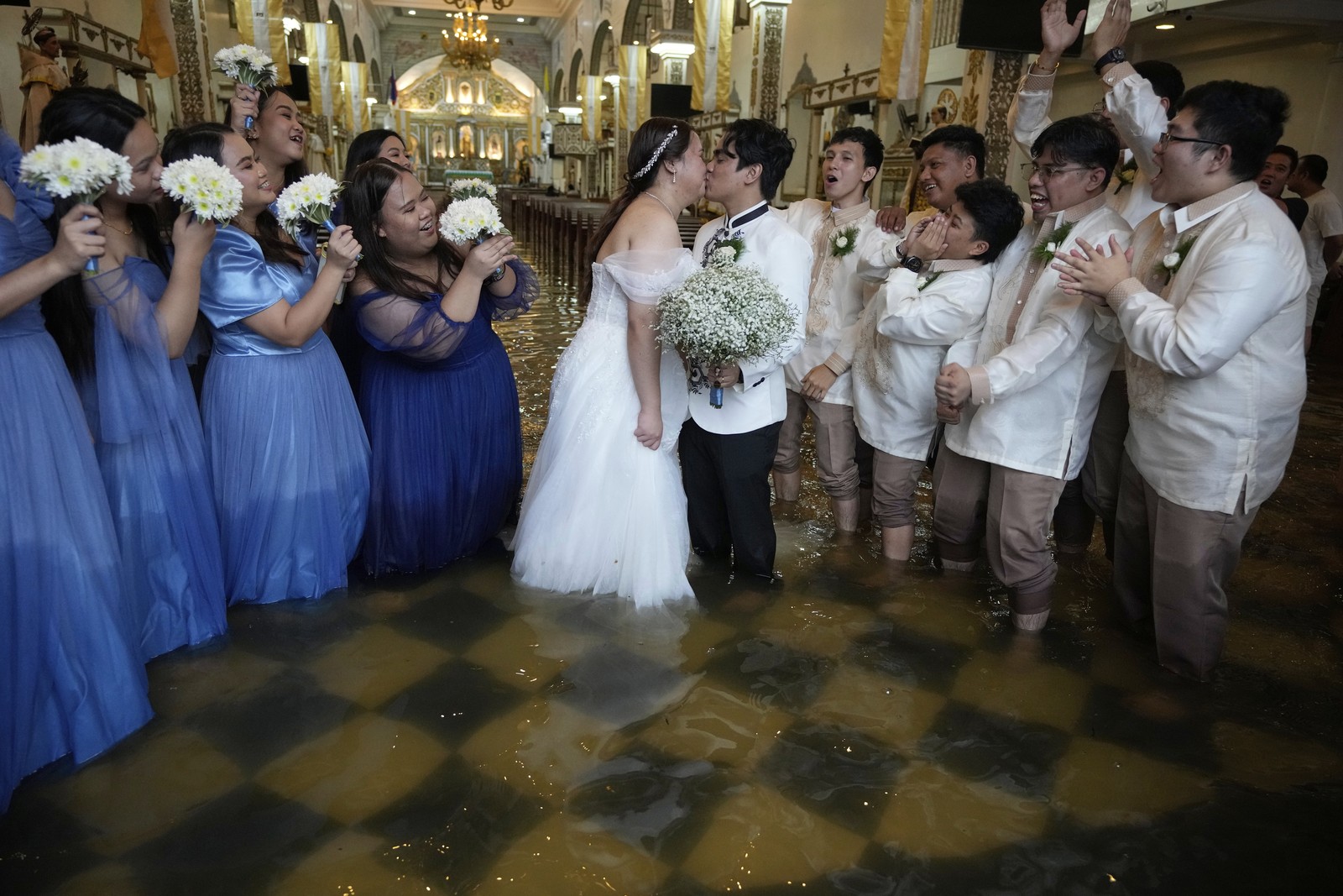 Guests cheer as a newlywed couple shares a kiss inside a flooded church.