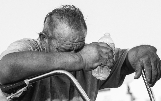 A man holding his head down, grasping a water bottle