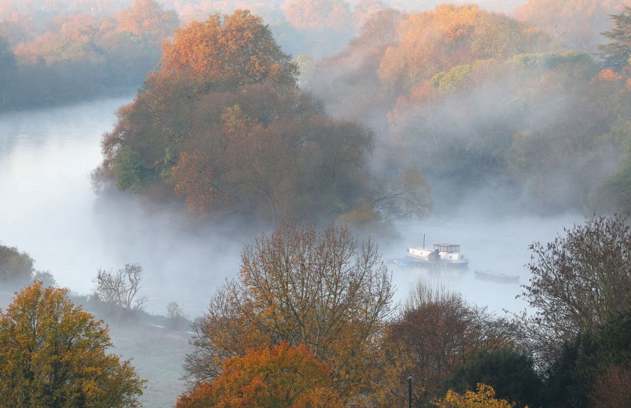 A barge sits in a river, surrounded by autumn-colored trees on a misty morning.