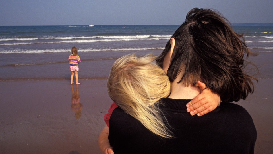 A woman holding a child and standing near another child, all by the ocean