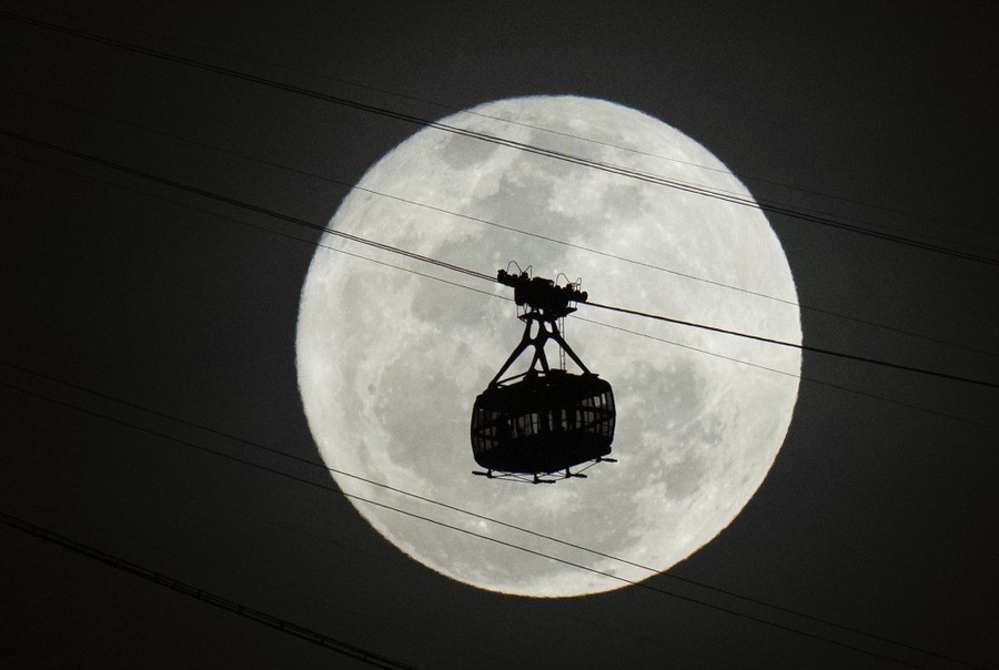 A cable car is seen in silhouette in front of a full moon.