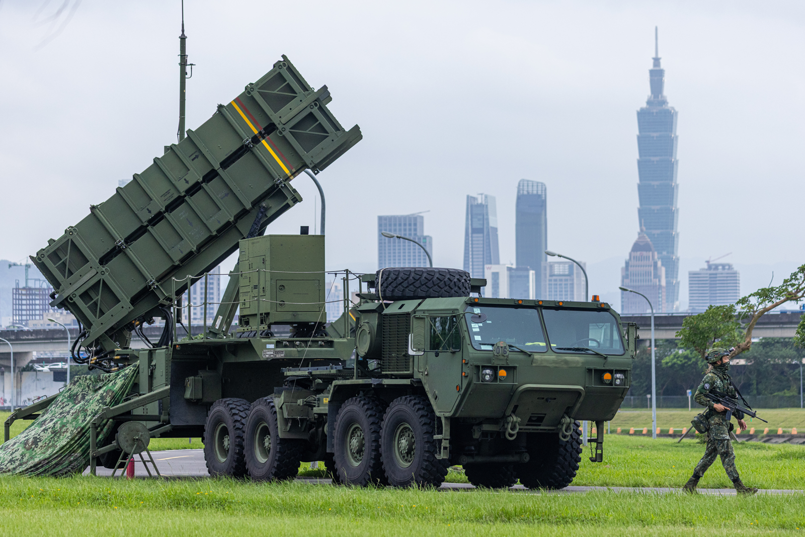 photo of large green military truck with armed soldiers and Taipei skyline in background