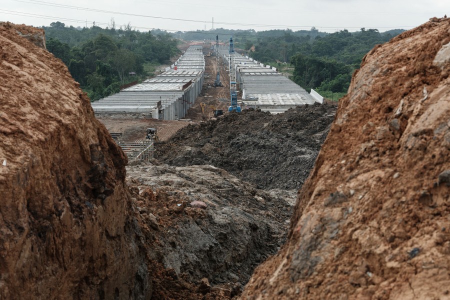 A highway under construction, surrounded by trees and piles of dirt