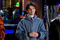 Actor Timothée Chalamet, wearing a blue-colored zip-up hoodie, stands with his hands clasped at his chest.