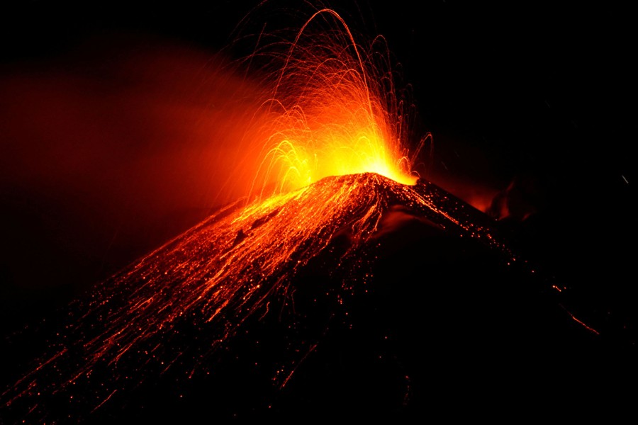 Lava shoots from the top of a volcano at night.