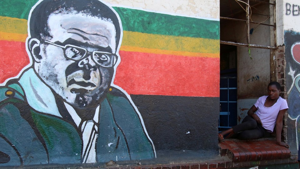A woman sits next to a mural depicting Robert Mugabe.