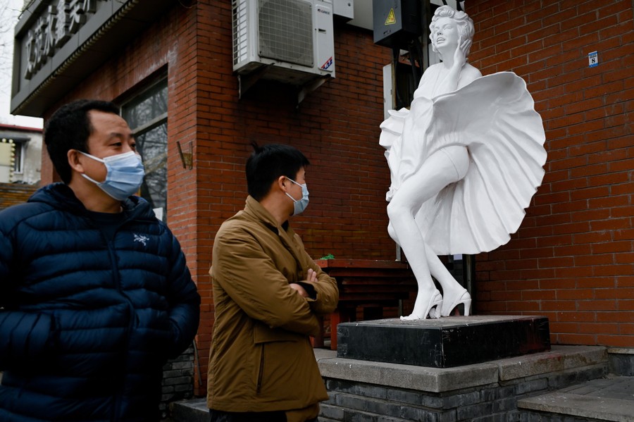 Two people walk on a sidewalk beside a statue depicting Marilyn Monroe in a famous scene from the 1955 movie "The Seven Year Itch."