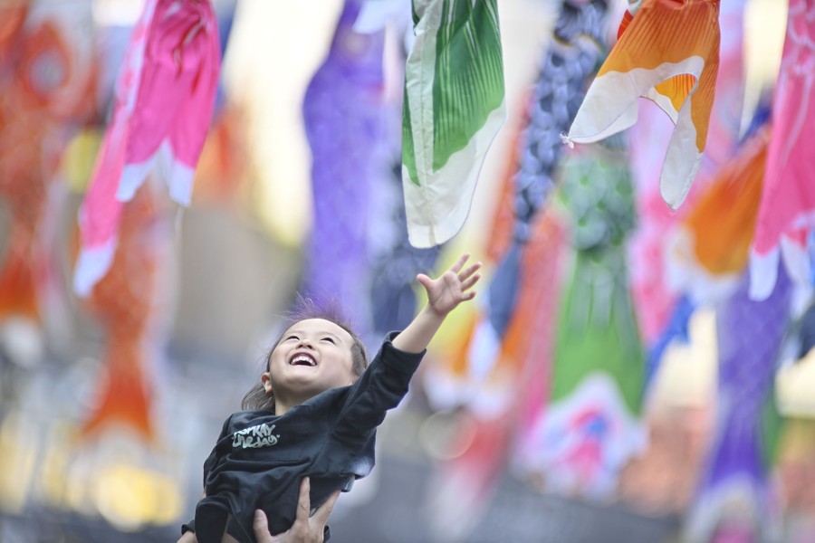 A young child is held high, reaching up toward banners hanging above.