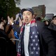Andrew Yang high fives a supporter at a rally. An American flag is draped over his neck.