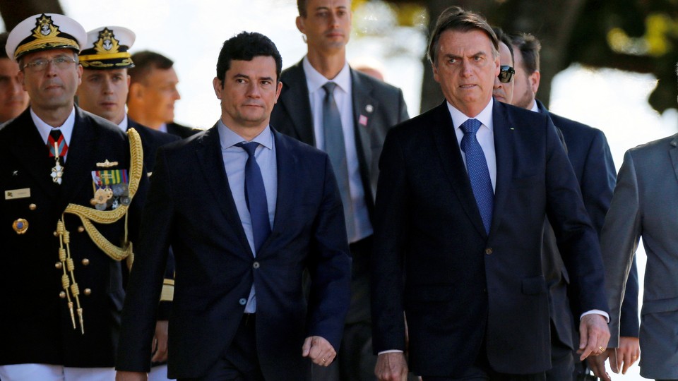 Sérgio Moro and Jair Bolsonaro walk with marines at a military ceremony.