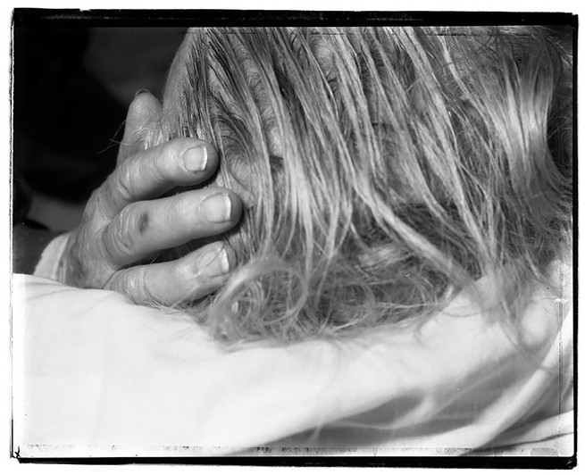 A wrinkled hand touches a head of gray hair.