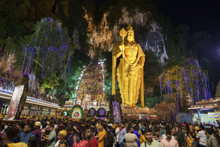 A large crowd of people walk beside a tall golden statue.