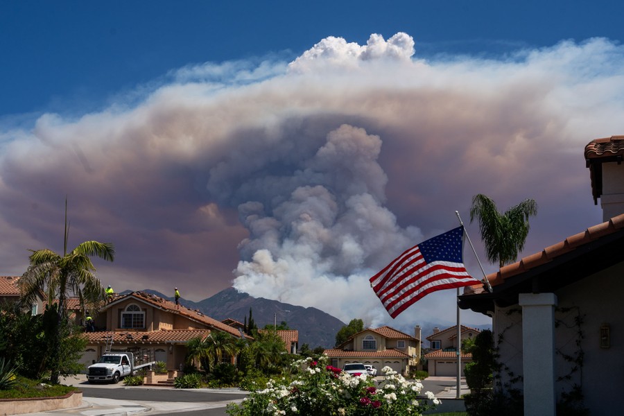 A plume of thick smoke rises from a wildfire burning near a residential area.