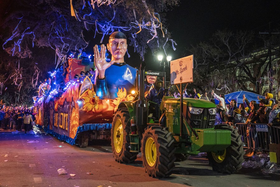 A tractor pulls a parade float featuring a Mr. Spock sculpture past a crowd.