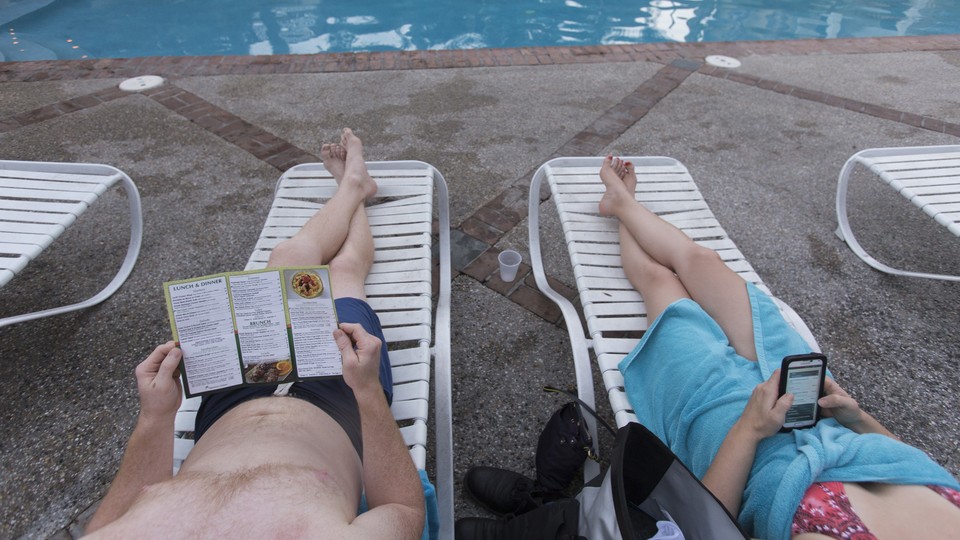 Two people sit in lounge chairs by a pool