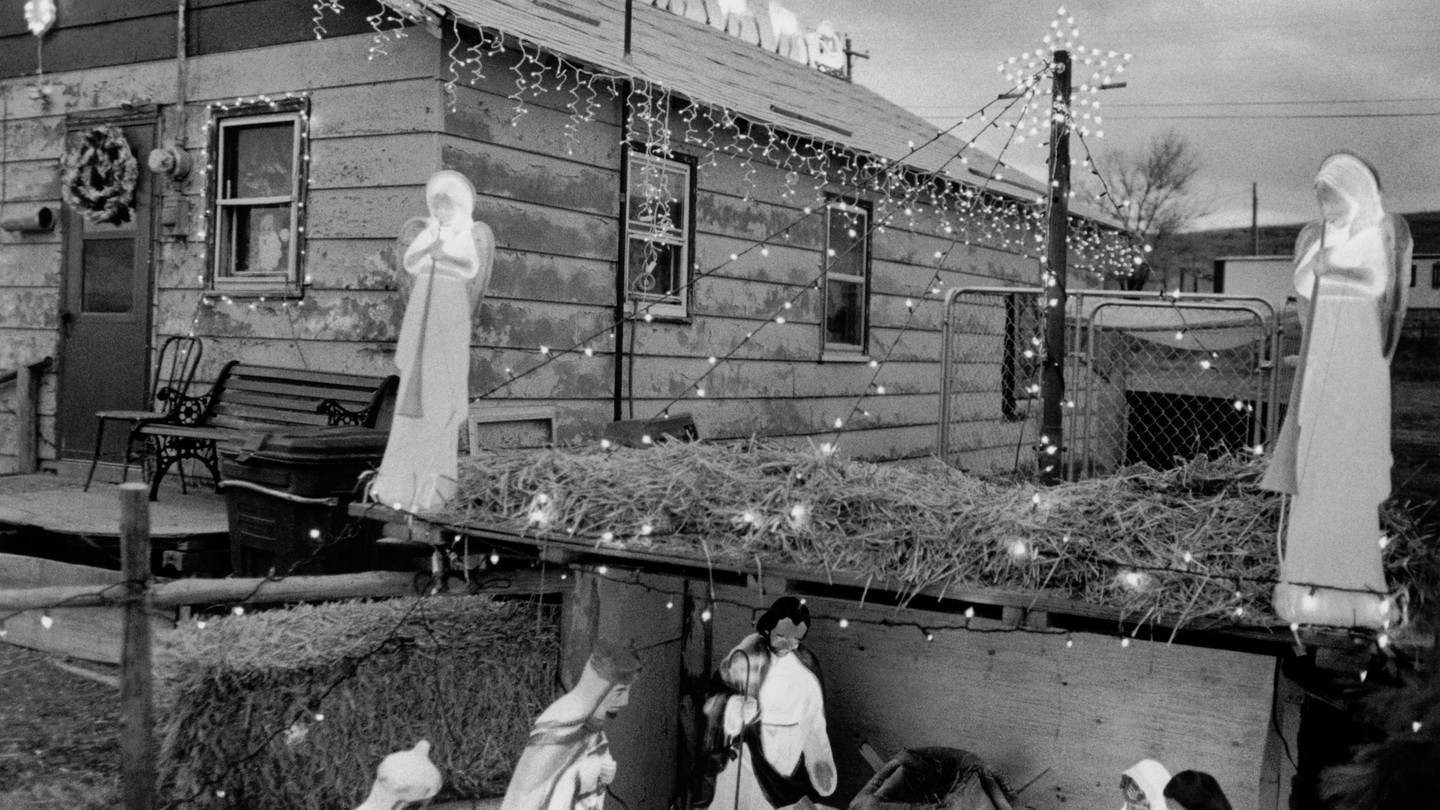 A photo of a small, one-story house strung with Christmas lights. Next to it is a nativity scene and two angels flanking each side.