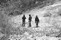 Black-and-white photo of three Israeli soldiers standing near circular barbed-wire fencing