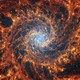 A tight view of a face-on spiral galaxy anchored by a central region that has a light-blue haze, surrounded by complex orange-colored spiral arms