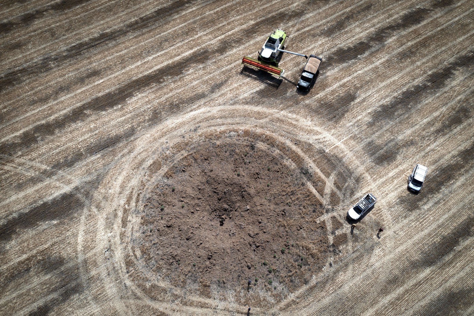 An aerial view of farm vehicles in a field near a fresh crater left by a Russian rocket.