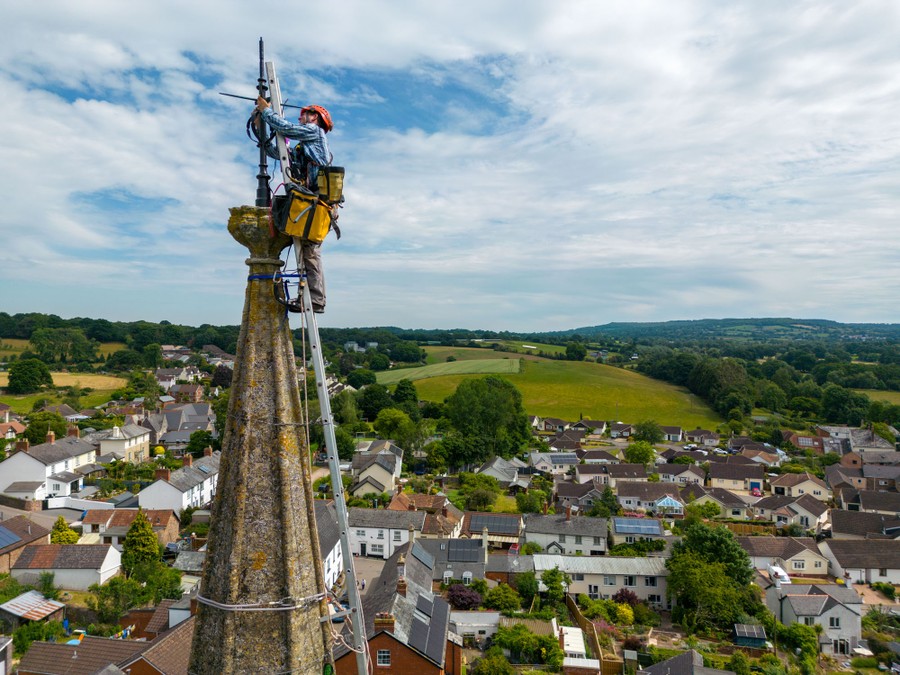 A person paints a lightning conductor at the tip of a tall church steeple.