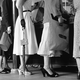 A black-and-white vintage photo of people wearing dresses, waiting in line