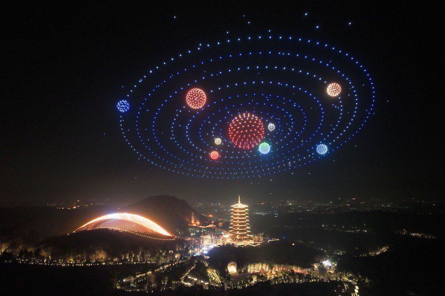 Illuminated drones form an image of a solar system above a pagoda at night.