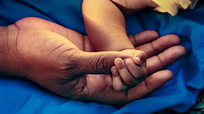 A baby's hand holds an adult's thumb