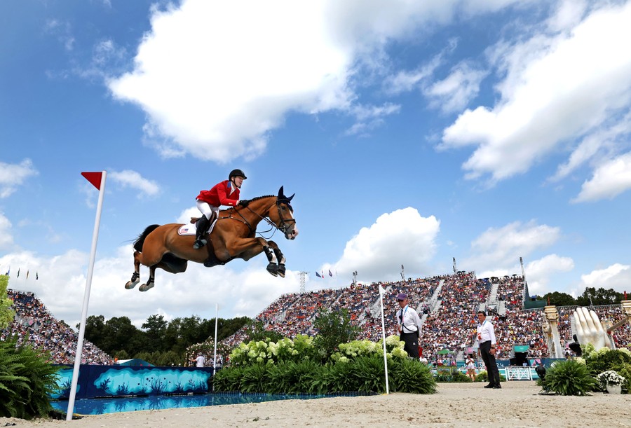 A rider holds on as a horse makes a long jump over an obstacle in a stadium.