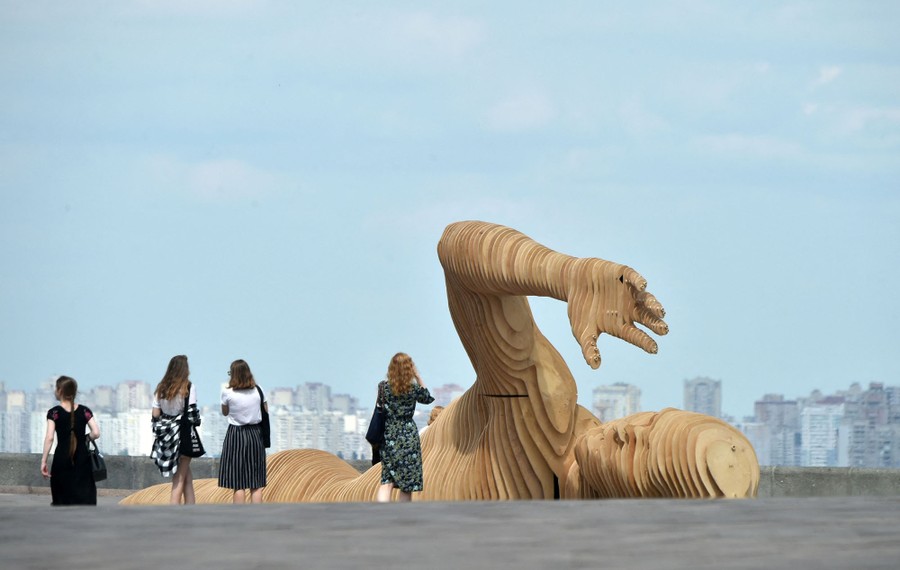 Four people walk near a large wooden statue of a swimmer.
