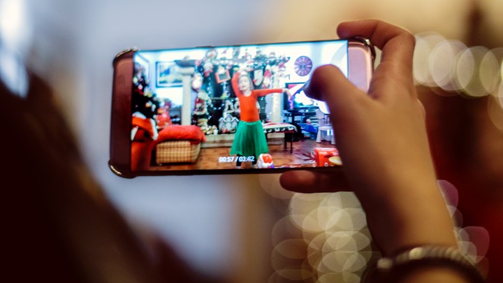 A person uses a smartphone to take a video of a child.