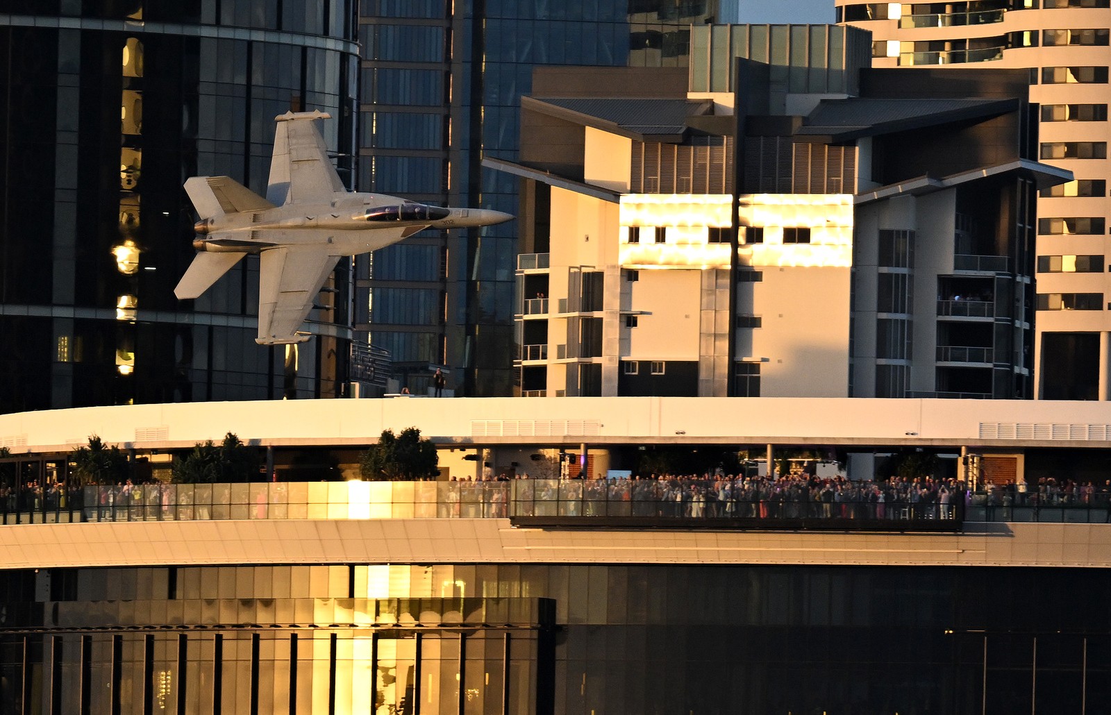 A fighter jet flies low, close to buildings, during a festival.