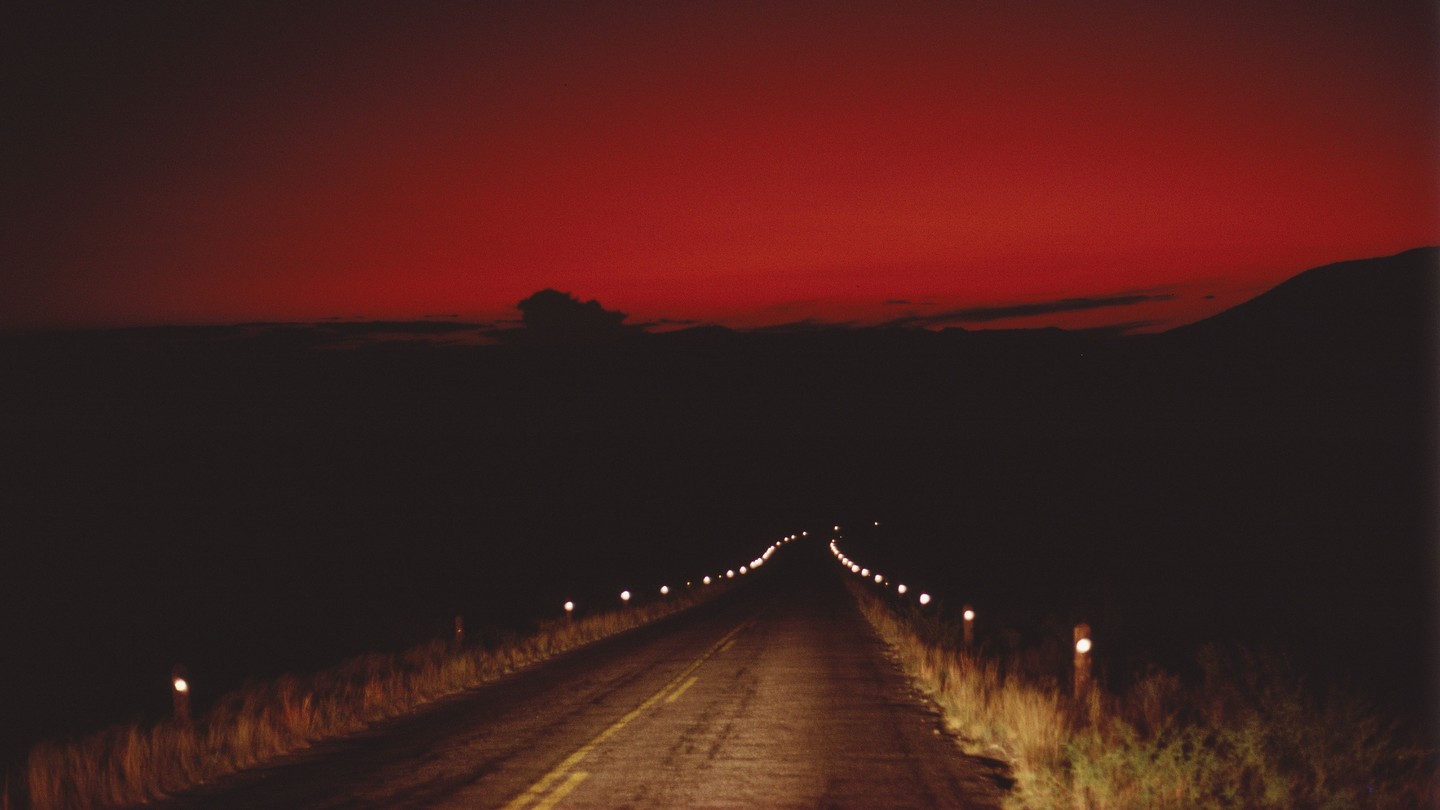 A photograph of a road going into Big Bend National Park during near dark, under a red sky