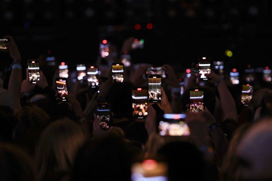 Many people in a crowd hold up their phones to record a concert.