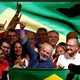 A man raises his fist on a stage among and in front of cheering supporters.