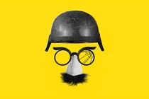 A military helmet floats above disguise glasses with fake nose and mustache. One lens of the glasses is shattered.