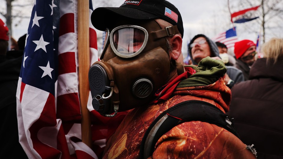 An insurrectionist wearing a gas mask and holding an American flag on January 6 