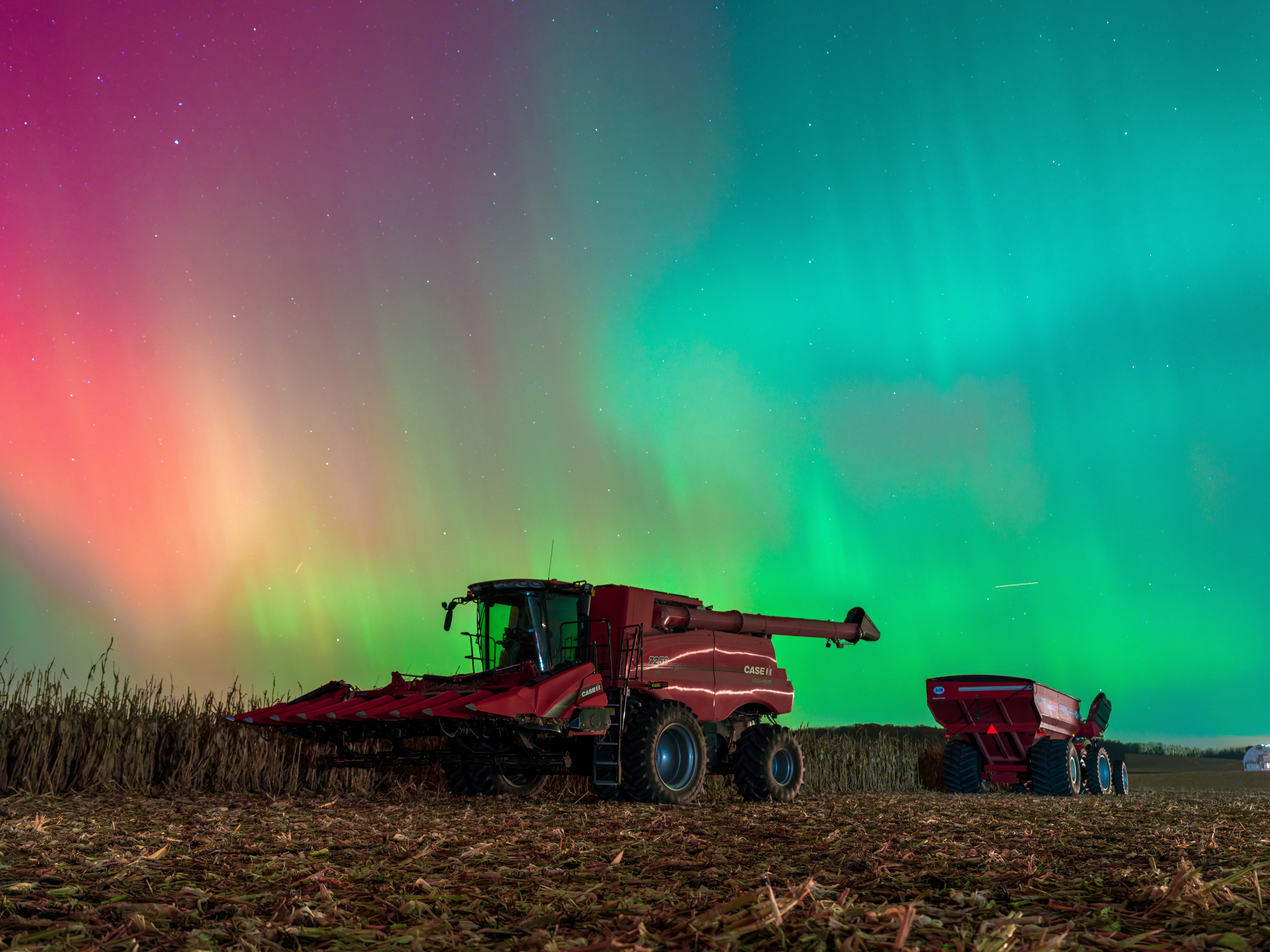 Green and red curtains of light hang in the night sky above farm equipment in a field.