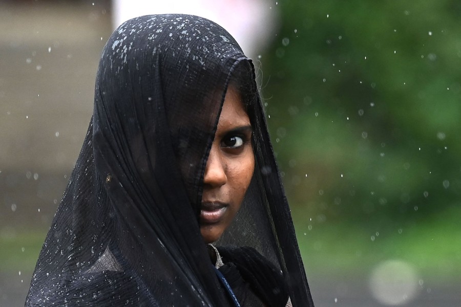A woman is outside on a rainy day, looking toward the camera while wearing a head covering.
