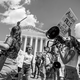 Black-and-white photo of anti-abortion protesters drumming and shouting through bullhorns in front of the Supreme Court, holding signs, including one that reads "Abortion PILLS are MURDER!"