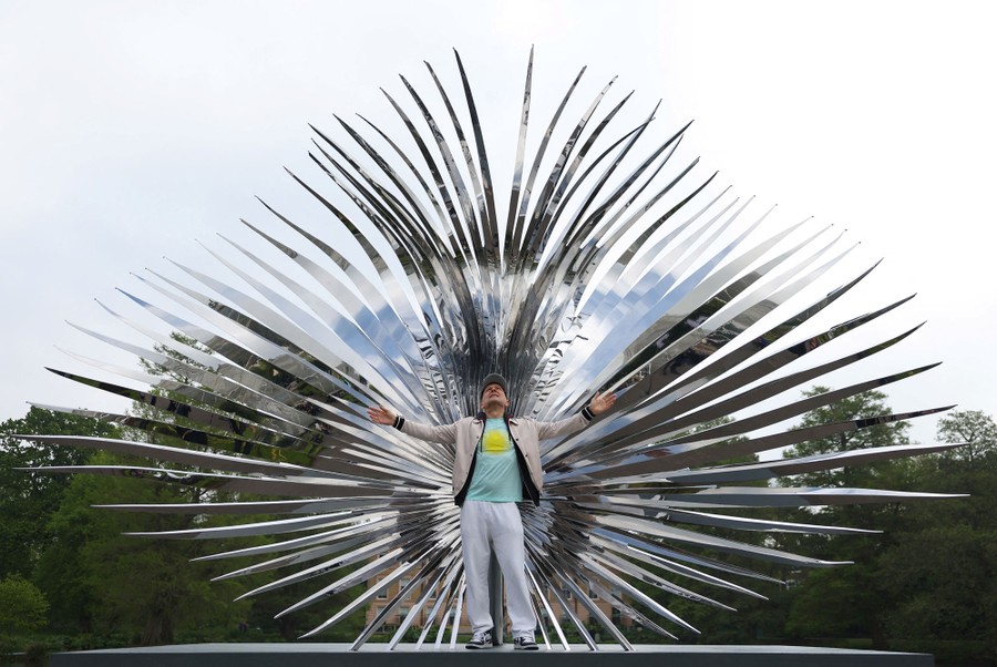 A person stands in front of a large outdoor art installation made up of many mirror-finish spikes radiating out from a cluster.