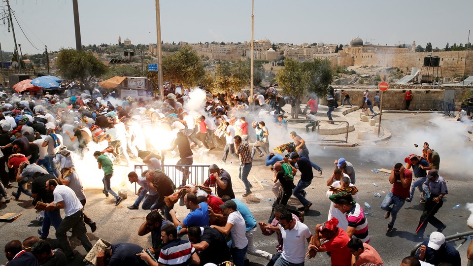 Palestinians react following tear gas that was shot by Israeli forces after Friday prayer on a street outside Jerusalem's Old city .