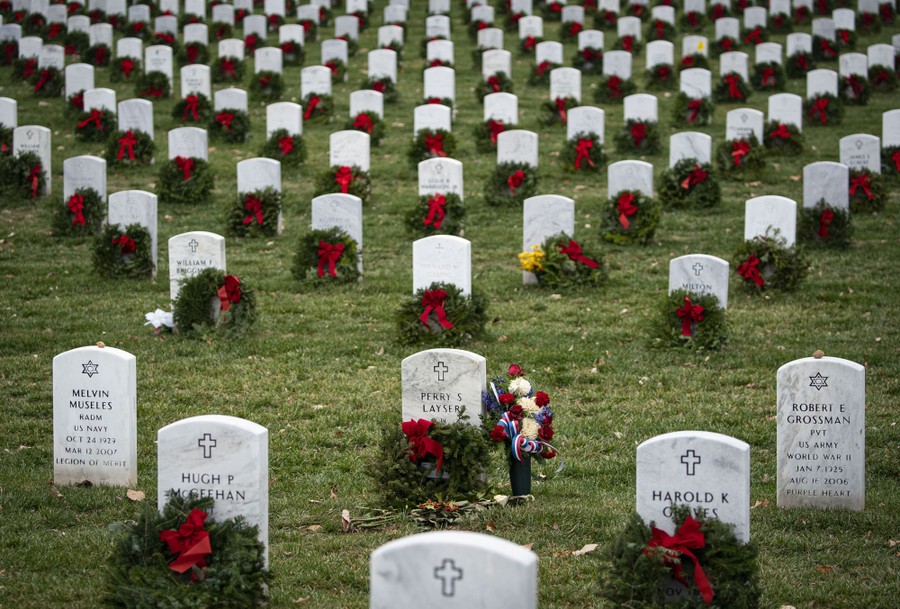 Wreaths with red ribbons lean against hundreds of tombstones.