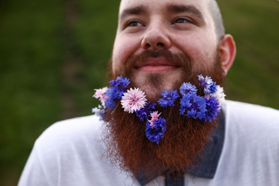 A man smiles, with many small flowers placed in his beard.