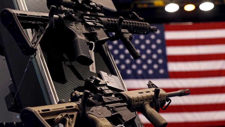 A photograph of two assault rifles on a store shelf, with the American flag visible behind them.