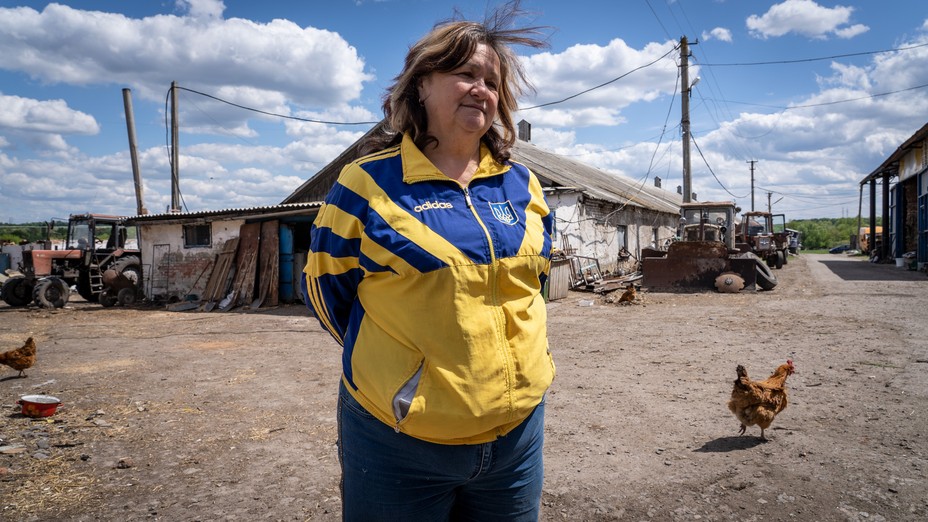 A woman wearing a yellow and blue jacket stands in front of a building in a village.