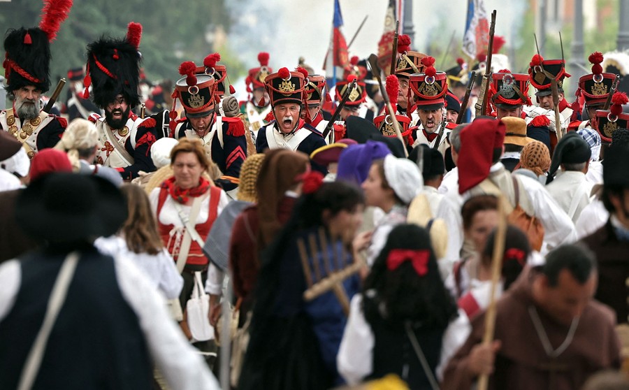 People wearing historical soldiers' uniforms and other costumes perform a reenactment.