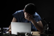 A doctor at a desk with his head in his hands